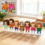 Custom brick figures of a large family lineup displayed on a base, inspired by a reference family photo shown in the corner, placed on a table in a bright home setting