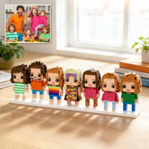 Custom brick figures of a large family lineup displayed on a base, inspired by a reference family photo shown in the corner, placed on a table in a bright home setting
