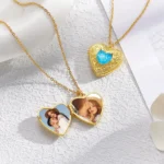 Gold heart locket necklaces with blue gemstone detail, one open showing personalized couple photos inside and one closed, placed on a textured white surface