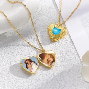 Gold heart locket necklaces with blue gemstone detail, one open showing personalized couple photos inside and one closed, placed on a textured white surface