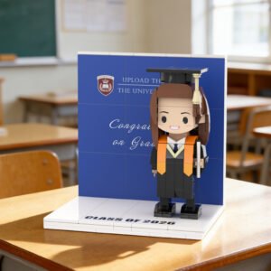 Custom brick figure of a female graduate in cap and gown holding a diploma, displayed on a base with “Class of 2026” and a congratulatory graduation backdrop in a classroom setting