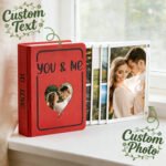 Customizable photo album with a red cover featuring the words 'You & Me' and a heart-shaped cutout. The album includes custom text and photos, showcasing a couple's image on the front page