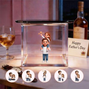 A personalized 3D holographic figurine of a father carrying his daughter on his shoulders inside a glass display box. Surrounding the display are smaller circular images showcasing different poses of the father and daughter. A 'Happy Father's Day' card sits next to a bottle of whiskey, with a glass of whiskey on the table, accompanied by a wristwatch