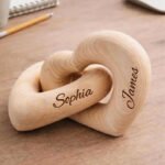 Personalized wooden interlocking heart sculpture engraved with the names Sophia and James, placed on a wooden desk