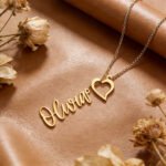 Personalized gold name necklace with heart pendant, featuring the name Olivia, placed on a leather background with dried flowers
