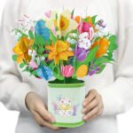 Decorative Easter bouquet with paper flowers and bunnies in a pastel gift bucket being held by a person.