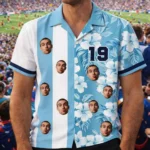 "A custom blue and white floral shirt with multiple small faces of a man on it, paired with the number '19' on the front. The shirt has a sporty, tropical design, and the background shows a blurred crowd at a sports event."