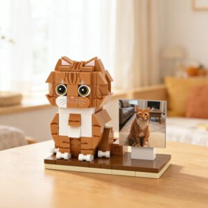 Custom brick-built cat figure model with a photo reference display, designed to resemble a real orange tabby cat, placed on a wooden table indoors