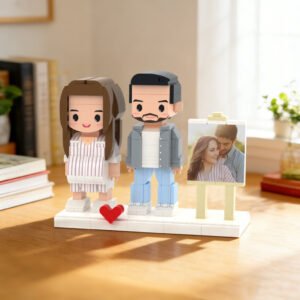 Custom brick figures of a couple standing on a base with a small heart detail, displayed with a reference photo on a stand in a cozy indoor setting