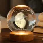 Personalized moon lamp with engraved text ‘Our Moon’ and names Sophia and Thomas with date, glowing inside a glass sphere on a wooden base
