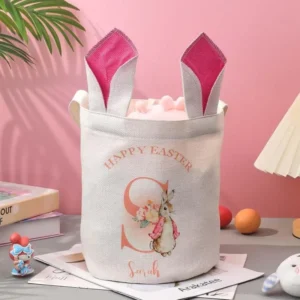 Personalized Easter basket with bunny ear handles, printed with ‘Happy Easter,’ a bunny illustration, and the name Sarah, filled with treats and placed on a pastel-themed table
