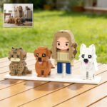 Custom brick figure of a woman with three pets (cat and two dogs) displayed on a base outdoors, with a reference photo of the owner and pets shown in the corner