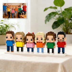 Custom brick figures of a group of six people displayed on a base, inspired by a family or friends photo shown in the corner, placed on a table indoors
